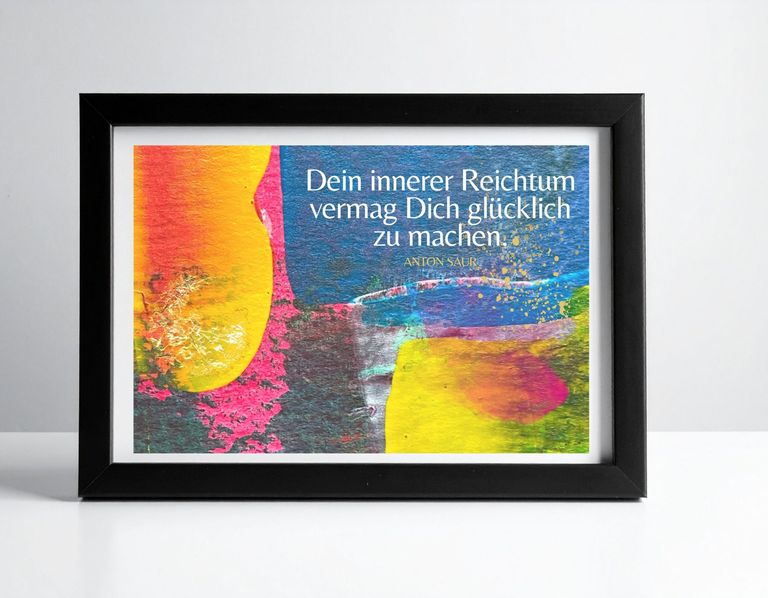 Ein schwarzer Bilderrahmen hält ein buntes Gemälde mit abstrakten Farbflächen in Gelb, Rot und Blau, auf dem ein Zitat von Anton Saur in weißer Schrift steht.